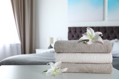 Photo of Stack of fresh towels with flowers on table in bedroom. Space for text
