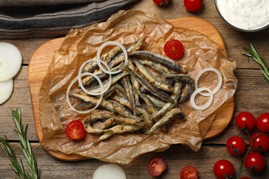Board with delicious fried anchovies, onion and tomatoes on wooden table, flat lay