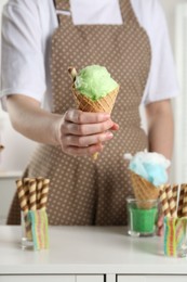 Photo of Woman holding waffle cone with cotton candy indoors, closeup