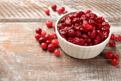Photo of Tasty dried cranberries in bowl and fresh ones on rustic wooden table. Space for text
