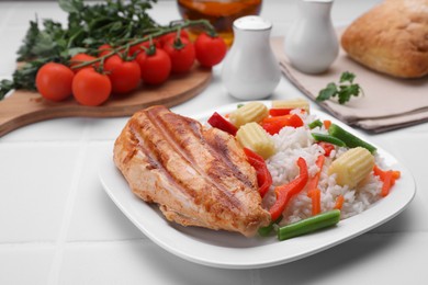Grilled chicken breast and rice served with vegetables on white tiled table