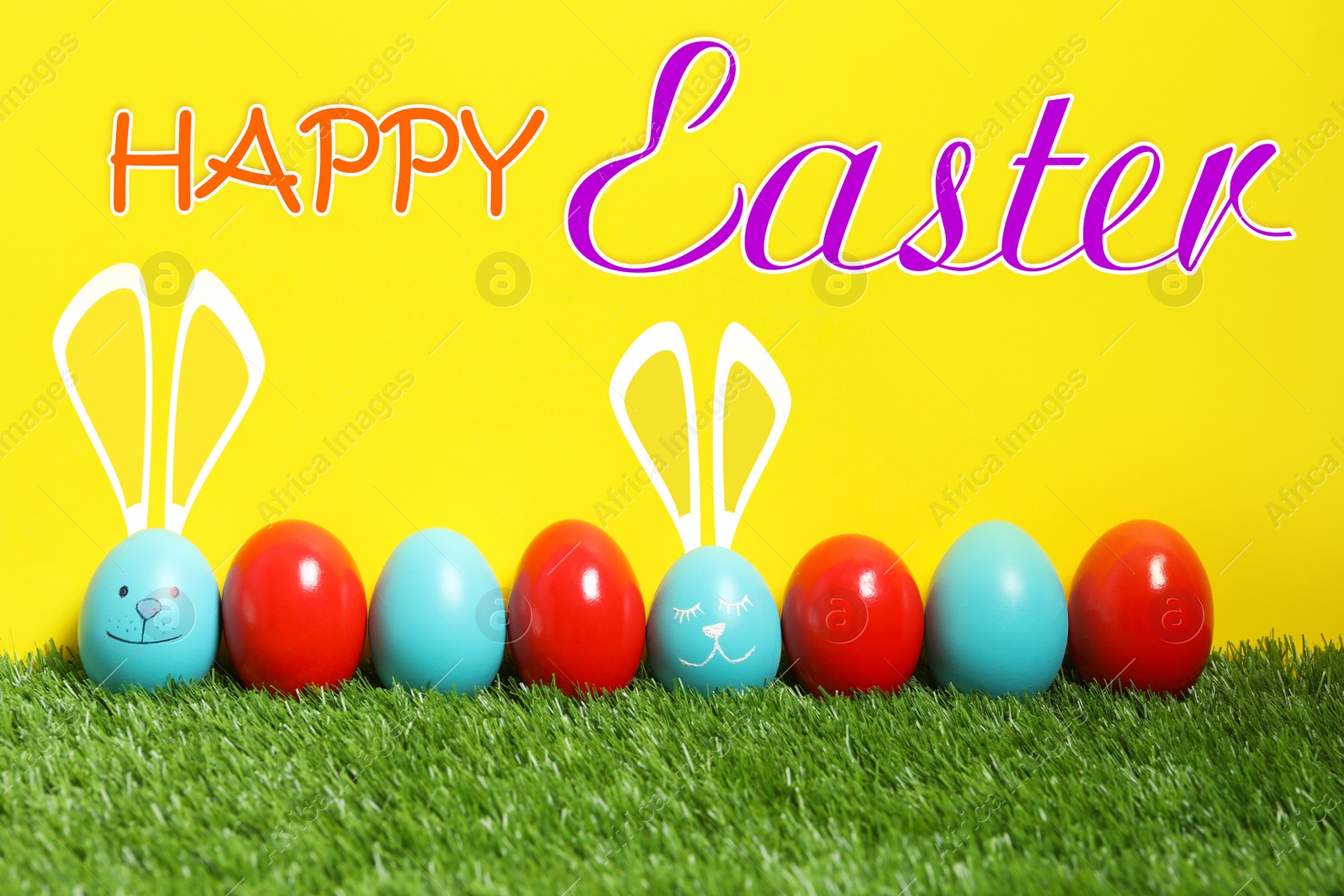 Image of Happy Easter. Two eggs with drawn faces and ears as bunnies among others on green grass against yellow background