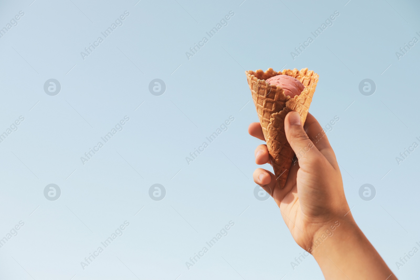 Photo of Woman holding delicious ice cream in waffle cone outdoors, closeup of hand. Space for text