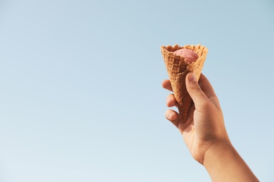 Woman holding delicious ice cream in waffle cone outdoors, closeup of hand. Space for text