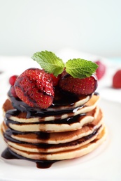 Delicious pancakes with fresh strawberries and chocolate syrup on table