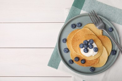 Photo of Tasty pancakes with natural yogurt and blueberries on white wooden table, flat lay. Space for text