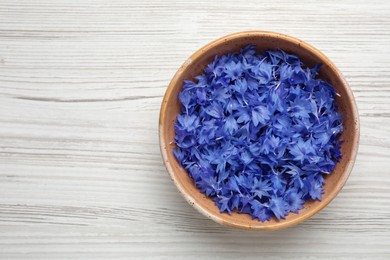 Photo of Beautiful blue cornflowers petals in bowl on white wooden table, top view. Space for text