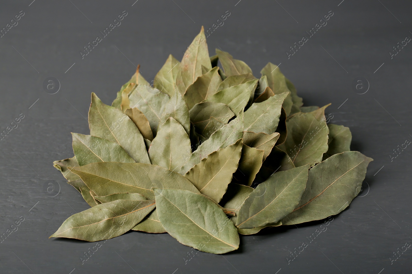 Photo of Pile of aromatic bay leaves on gray wooden table