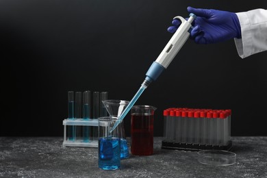 Laboratory analysis. Scientist dripping sample with micropipette into beaker at grey table, closeup