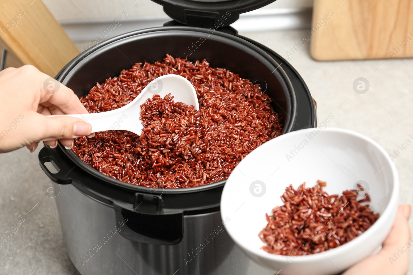 Photo of Woman putting brown rice into bowl from multi cooker in kitchen, closeup