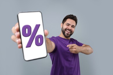 Image of Discount, offer, sale. Man pointing at mobile phone with percent sign on screen, grey background