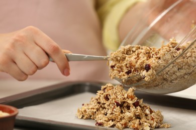 Photo of Making granola. Woman putting mixture of oat flakes, dried fruits and other ingredients onto baking tray, closeup