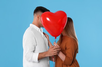 Lovely couple kissing behind heart shaped balloon on light blue background. Valentine's day celebration