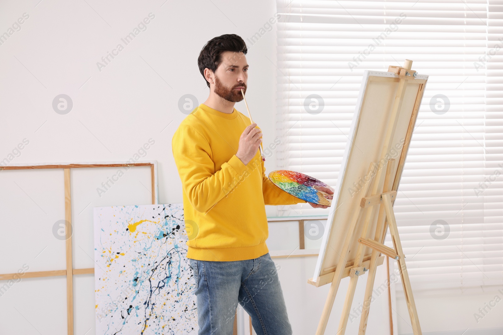 Photo of Man painting in studio. Using easel to hold canvas