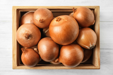 Ripe yellow onion bulbs in crate on white wooden table, top view