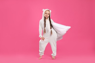 Photo of Cute girl wearing pajamas with pillow on pink background