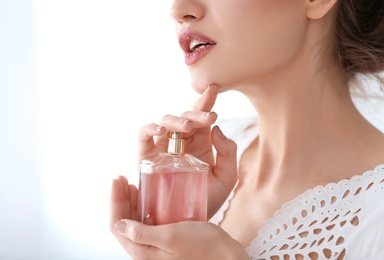Photo of Beautiful young woman with bottle of perfume on light background, closeup