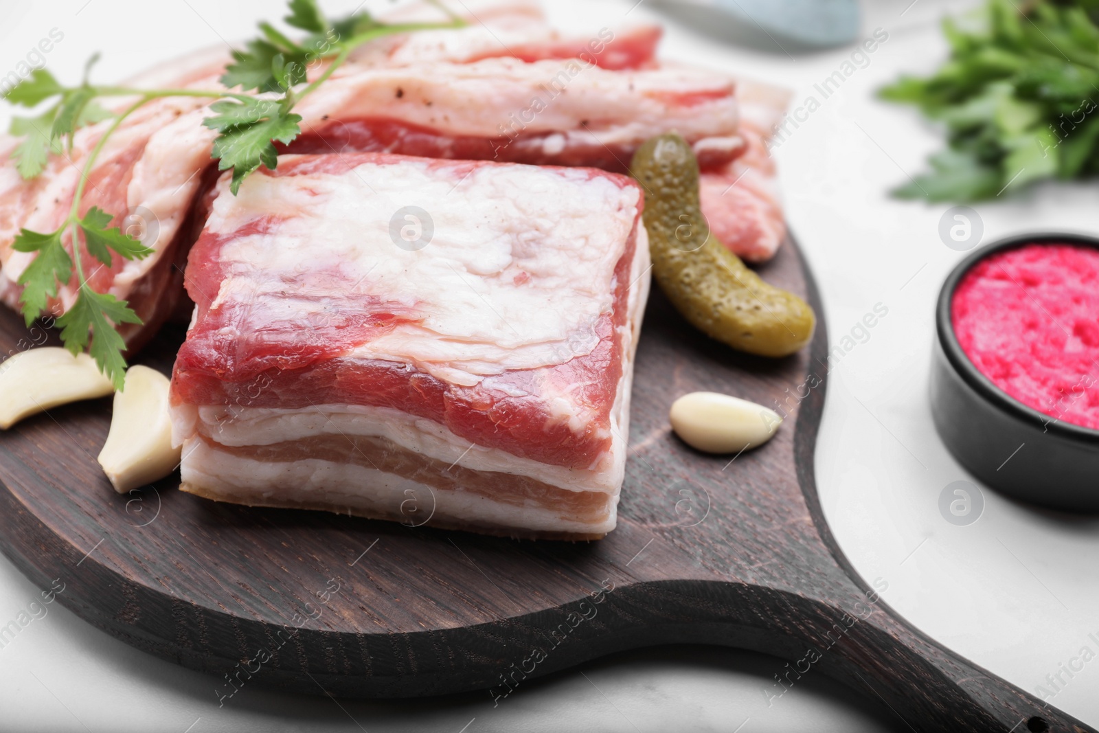 Photo of Tasty pork fatback with pickled cucumber, garlic and parsley on white table, closeup