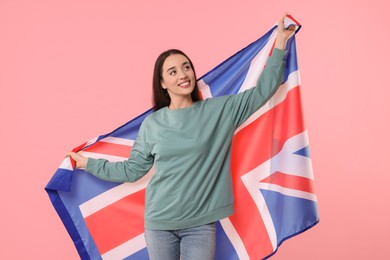 Young woman holding flag of United Kingdom on pink background