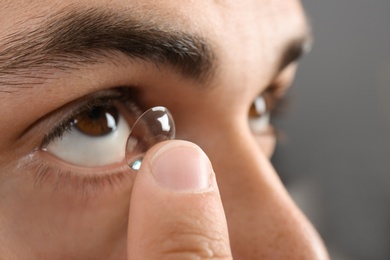 Young man putting contact lens into his eye, closeup