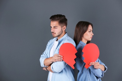 Young couple with torn paper heart on grey background. Relationship problems