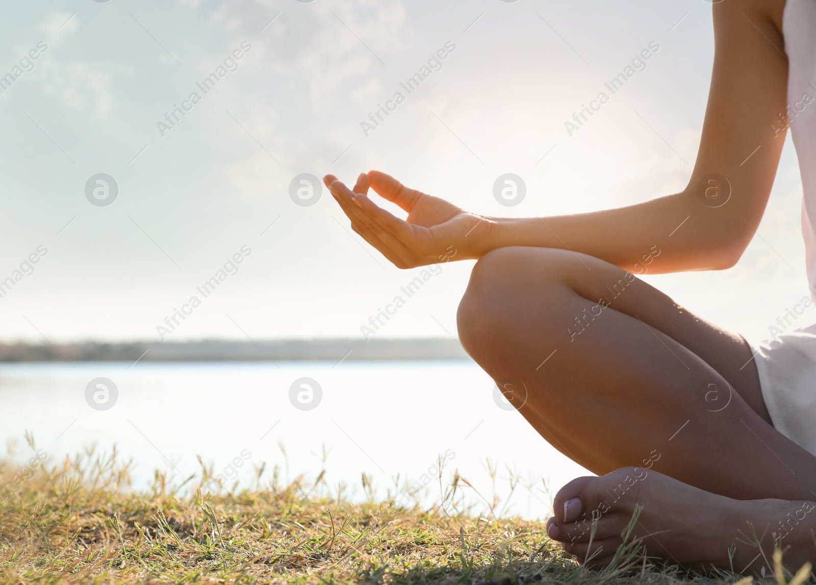 Photo of Young woman meditating near river at sunset, closeup view with space for text. Nature healing power