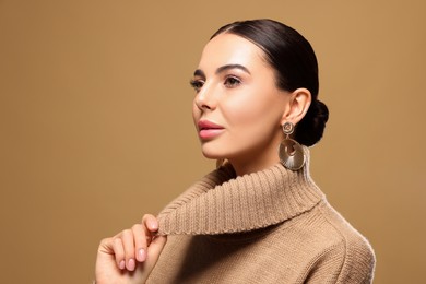 Photo of Beautiful young woman with elegant earrings on light brown background