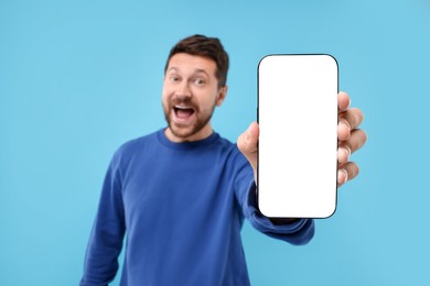 Surprised man showing smartphone in hand on light blue background, selective focus. Mockup for design