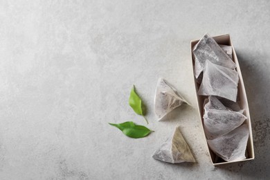 Photo of Box with tea bags and leaves on grey table, flat lay. Space for text