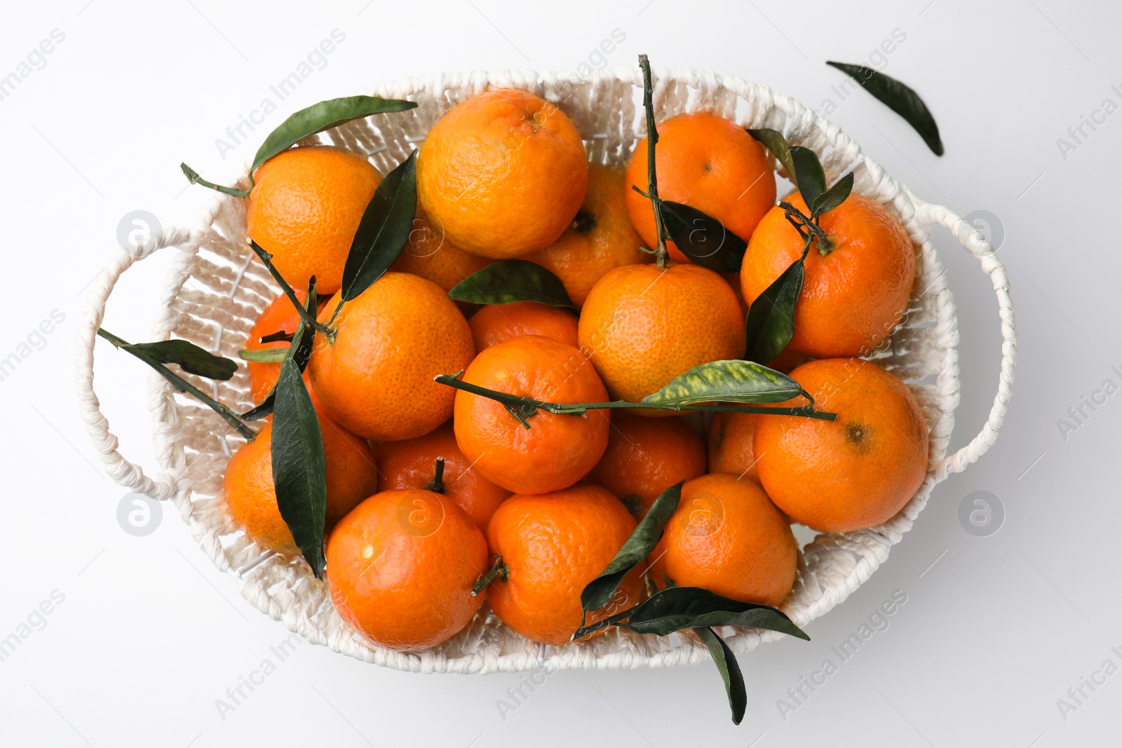Photo of Fresh ripe tangerines and leaves in basket on white table, top view