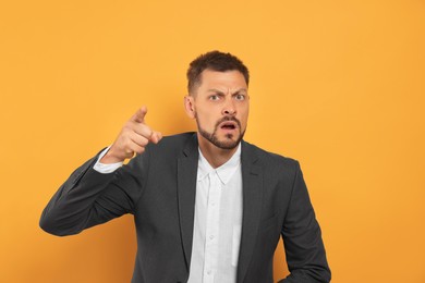 Photo of Aggressive man pointing on orange background. hate concept