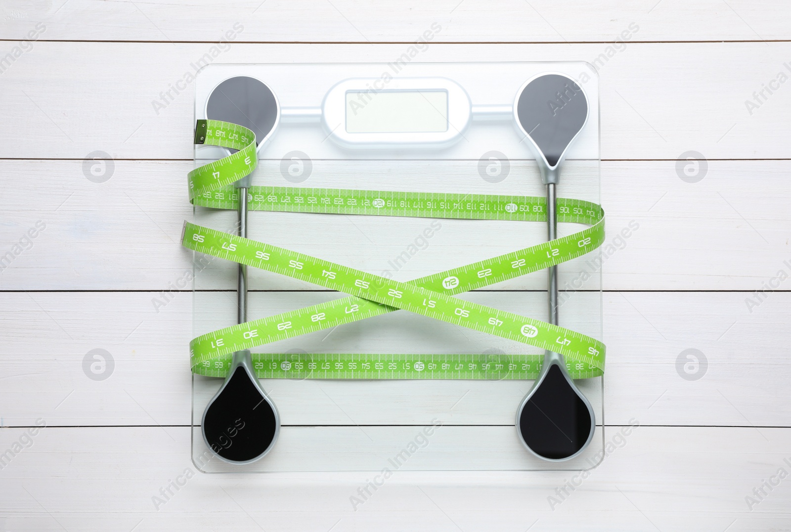 Photo of Bathroom scale and measuring tape on white wooden floor, top view. Weight loss concept