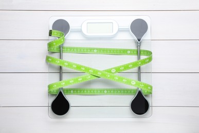 Photo of Bathroom scale and measuring tape on white wooden floor, top view. Weight loss concept