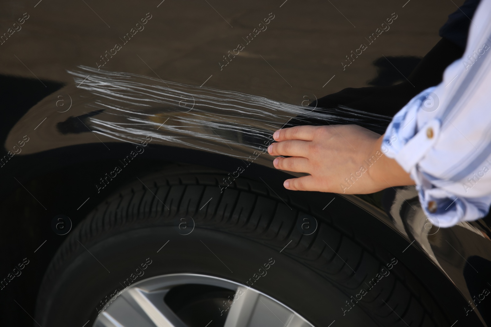 Photo of Young woman near car with scratch, closeup