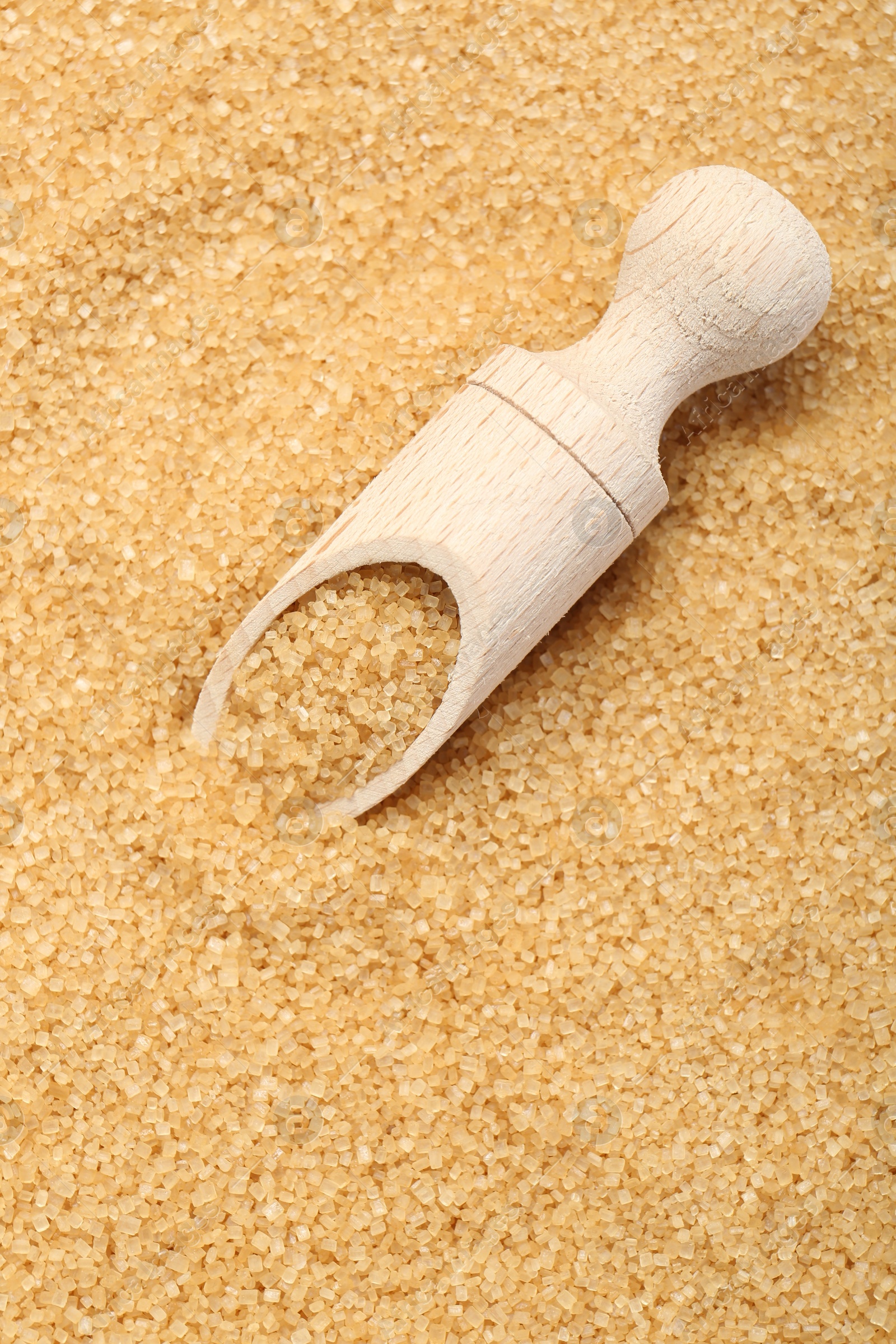 Photo of Wooden scoop on granulated brown sugar, top view