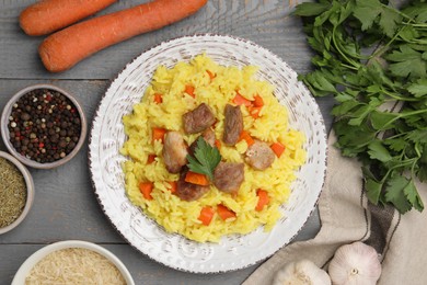 Photo of Delicious pilaf with meat and ingredients on grey wooden table, flat lay