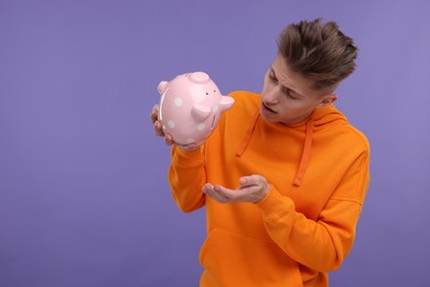 Photo of Upset man with piggy bank on purple background. Space for text