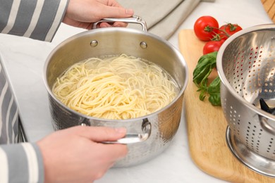 Photo of Woman with pot of cooked spaghetti at table, closeup