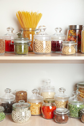 Photo of Glass jars with different types of groats and pasta on wooden shelves