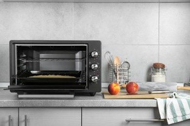 Photo of Open electric oven with dough on countertop in kitchen