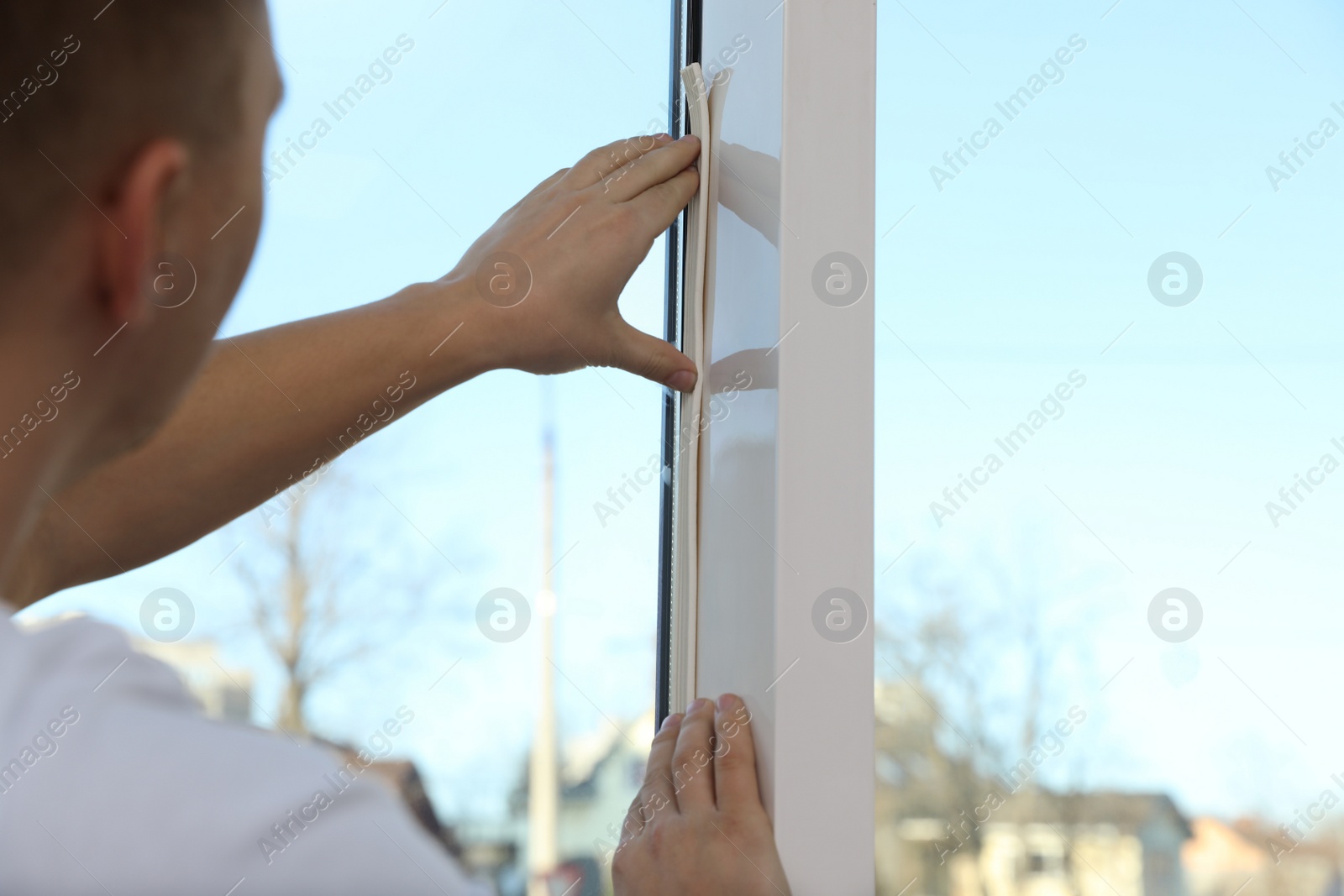 Photo of Construction worker putting sealing foam tape on window indoors, closeup