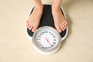Photo of Woman standing on floor scales indoors, above view. Overweight problem