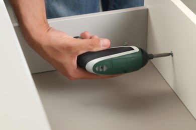 Photo of Man with electric screwdriver assembling drawer, closeup