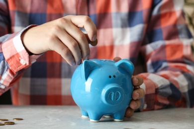 Photo of Man putting coin into piggy bank at grey marble table, closeup. Money savings