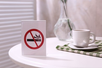 Photo of No Smoking sign and cup of coffee on white table indoors
