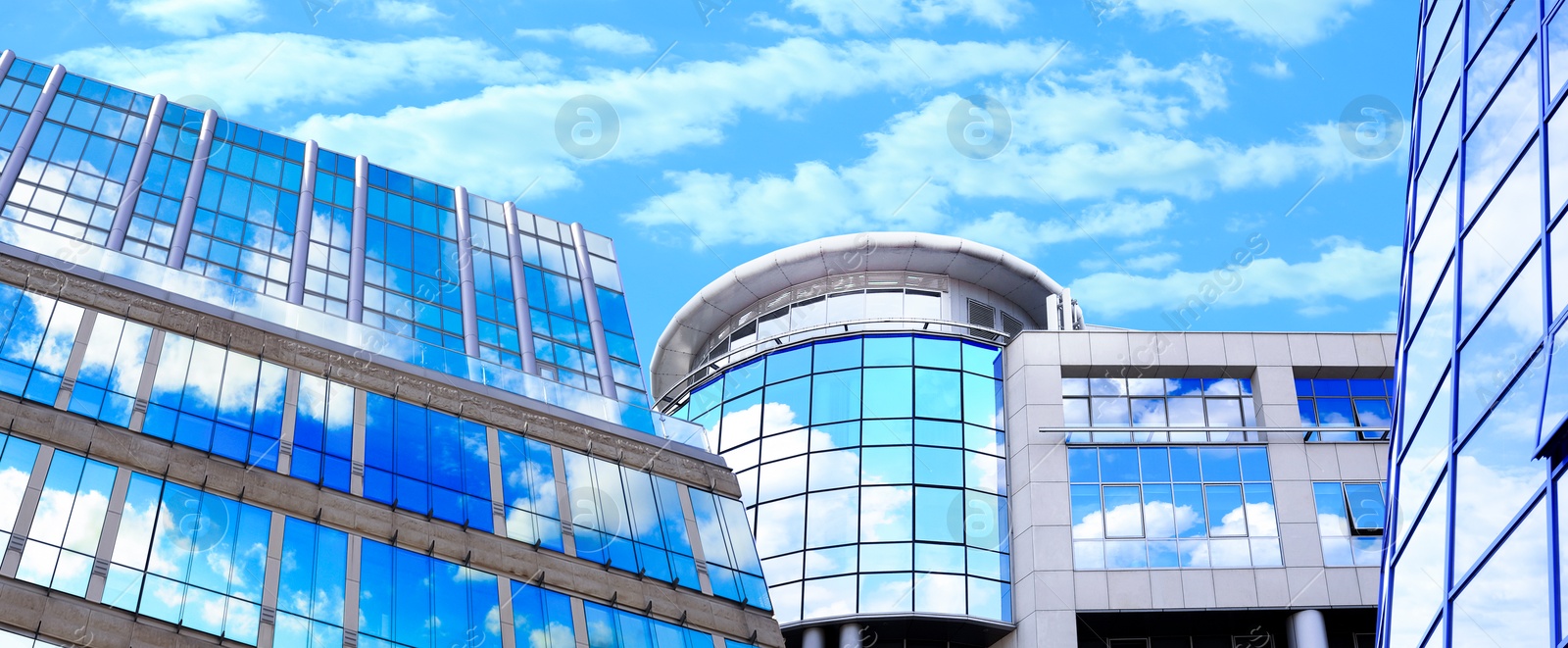 Image of Beautiful blue sky with clouds reflecting in windows of modern buildings, low angle view. Banner design