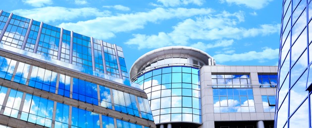 Image of Beautiful blue sky with clouds reflecting in windows of modern buildings, low angle view. Banner design