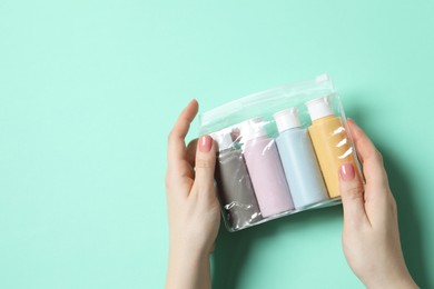 Photo of Cosmetic travel kit. Woman holding plastic bag with small bottles of personal care products against turquoise background, top view. Space for text