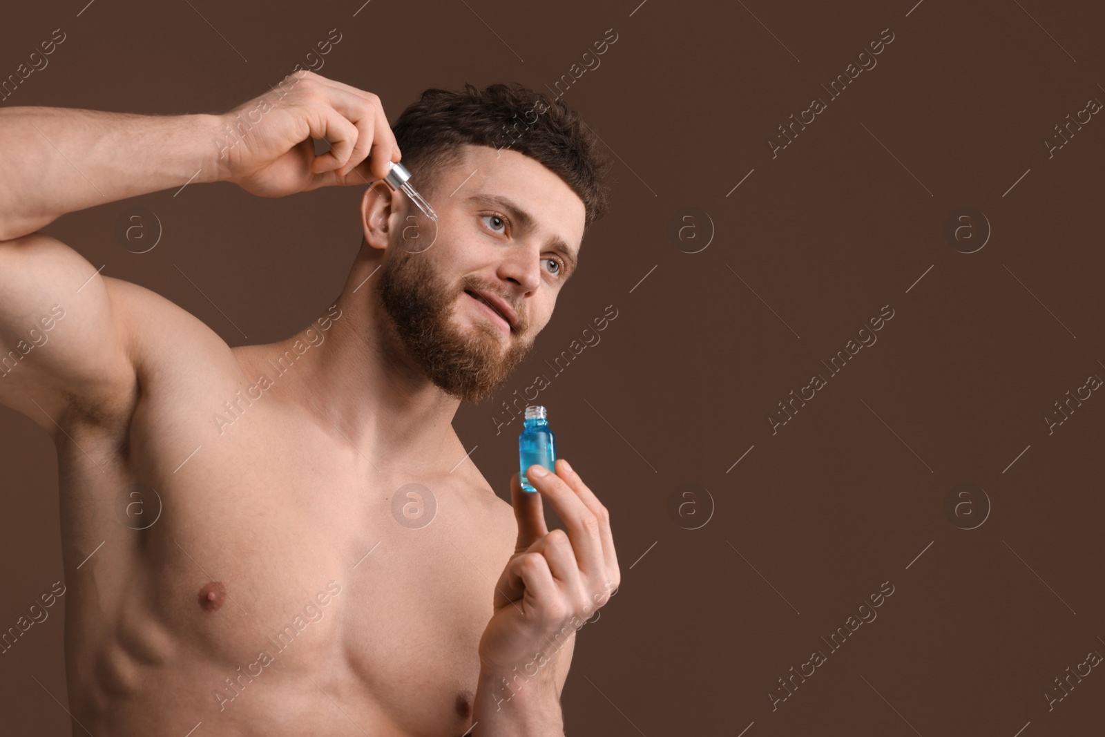 Photo of Handsome man applying serum onto his face on brown background, space for text