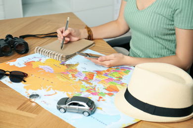 Woman with world map and smartphone planning trip at wooden table, closeup